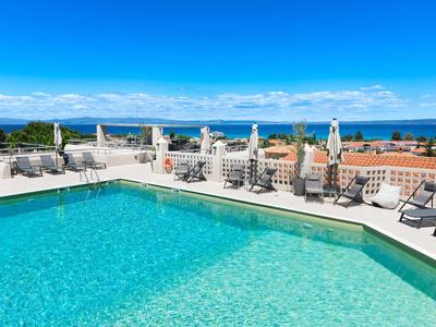 Large rooftop pool with lounge chairs and sea view under clear skies.