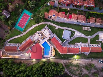Overview of a hotel with pool, tennis court, and parking in a green setting.