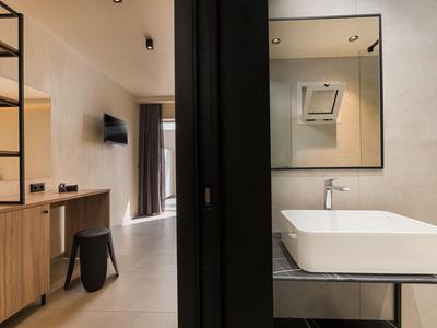 Moderní hotelový pokoj s dřevěnými policemi, televizí a koupelnou s obdélníkovým umyvadlem.