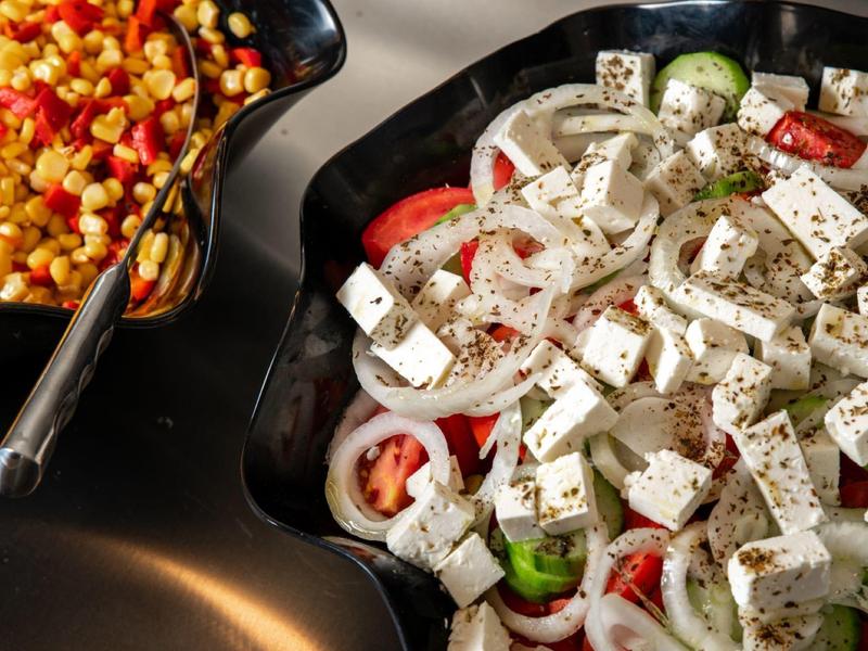 Salát s fetou a zeleninou vedle kukuřičného jídla v černých miskách.