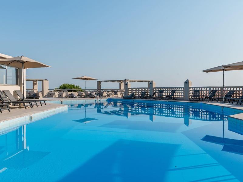 Čirý modrý bazén s lehátky a slunečníky za slunečného dne.