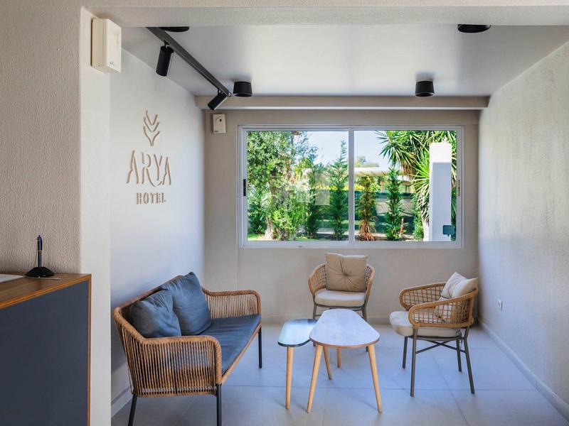 Světlý lounge kout s proutěnými křesly a stolky u velkého okna s výhledem na zahradu.