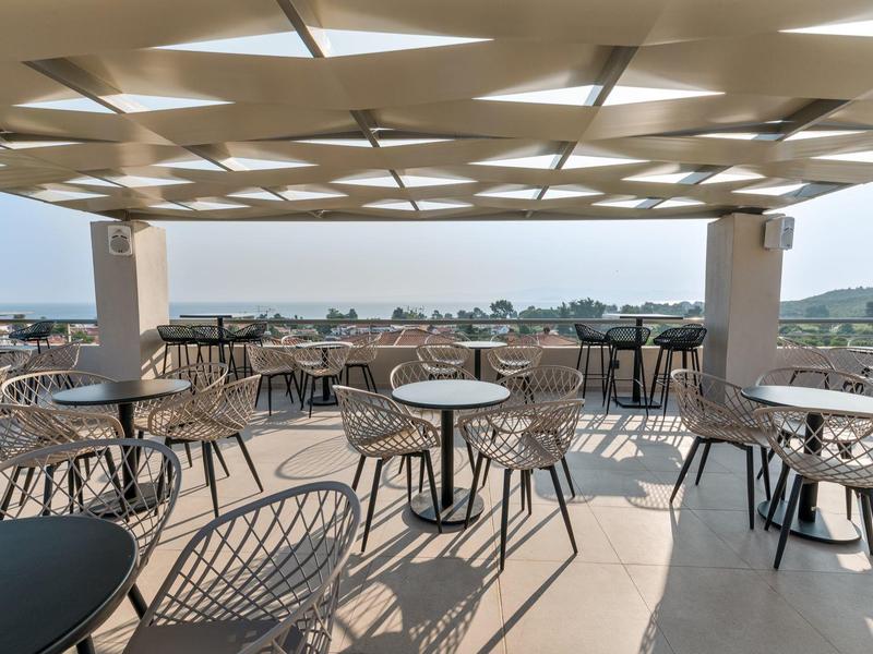 Slunečná terasa s stoly a židlemi s výhledem na moře a krajinu.