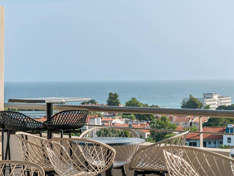 Balkon s židlemi a stoly s výhledem na moře a domy za ním.