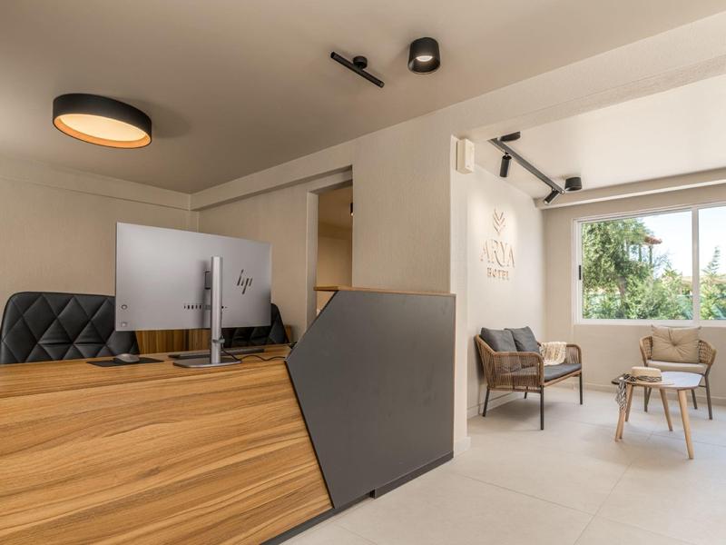 Moderní hotelová recepce s dřevěnou přepážkou a útulnou posezením u velkého okna.