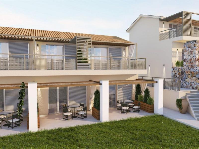 Moderní hotel se dvěma patry, prostornými balkóny a zeleným trávníkem v popředí.