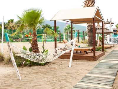 Plage avec sable, hamac et abri couvert sur passerelle en bois dans un hôtel.