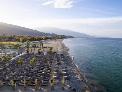 Strand mit Reihen von Sonnenschirmen und Liegestühlen neben ruhigem Meer und Bergen im Hintergrund