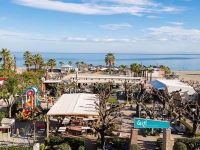Blick auf ein Strandrestaurant mit Spielplatz und Palmen am Meer unter blauem Himmel.