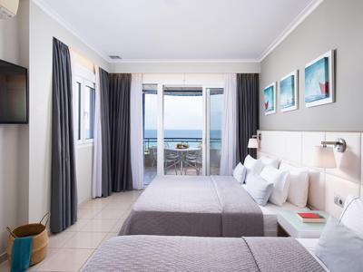 Modernes Doppelzimmer mit zwei Betten, Meerblick, Balkon, hellen Wänden und minimalistischer Einrichtung.