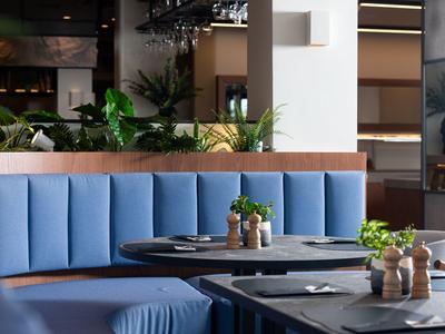 Elegantes Restaurant mit blauen Sitzbänken und dekorativen Pflanzen auf dunklen Tischen.