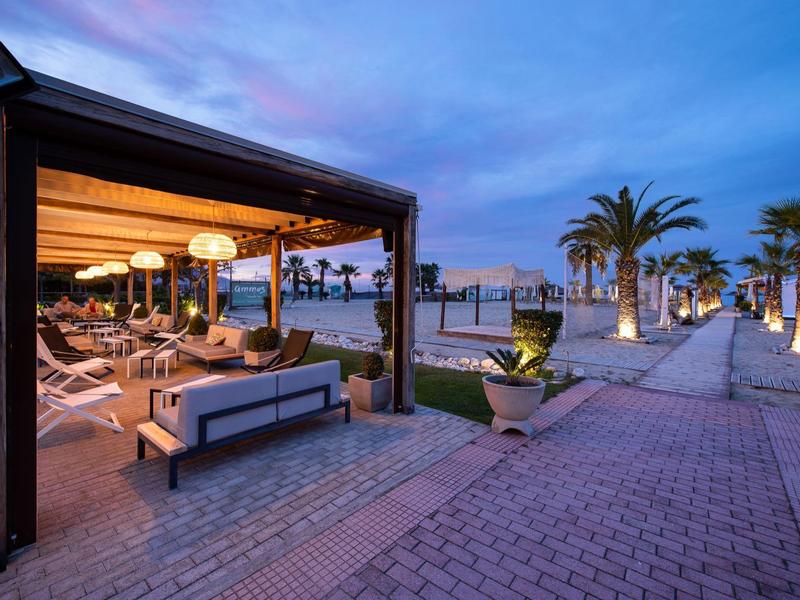 Moderner Strandpavillon mit gemütlichen Sitzmöbeln und Palmen bei Dämmerung am Meer.