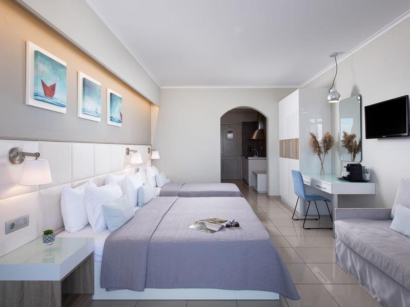 Modernes Hotelzimmer mit zwei Doppelbetten, grauen Decken, weißen Möbeln und Wandbildern.