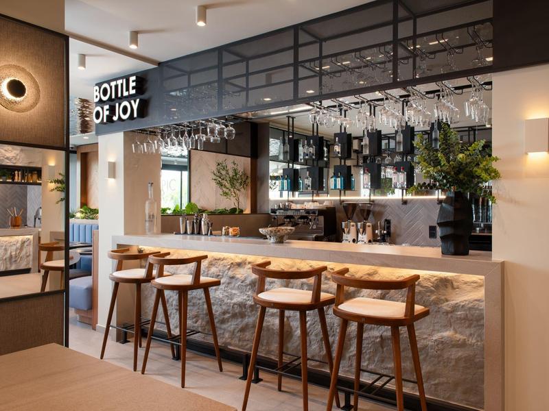 Moderner Barbereich mit hellem Steintresen, Holzstühlen und beleuchtetem Regal "Bottle of Joy".