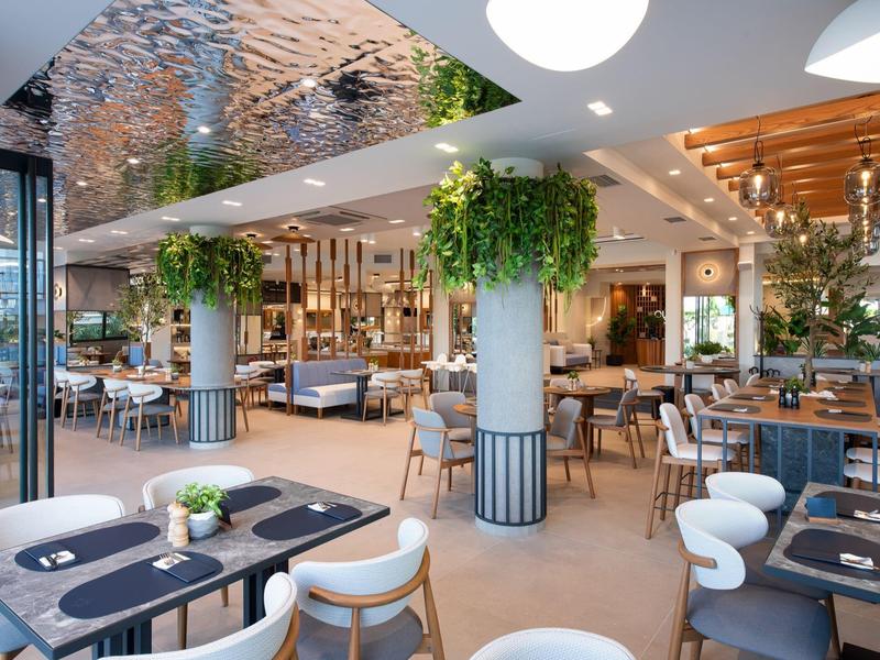 Modernes, helles Restaurant mit Holzdecken, vielen Pflanzen und stilvollen Sitzbereichen.