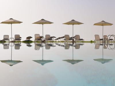 Disposition symétrique de quatre parasols et chaises au bord d'une piscine calme avec reflet.