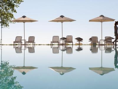 Trois parasols et plusieurs chaises longues au bord d'une piscine avec reflet dans l'eau.