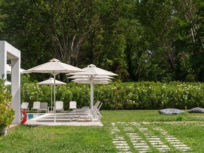 Espace jardin vert avec chaises longues blanches et parasols à côté d'un hôtel.