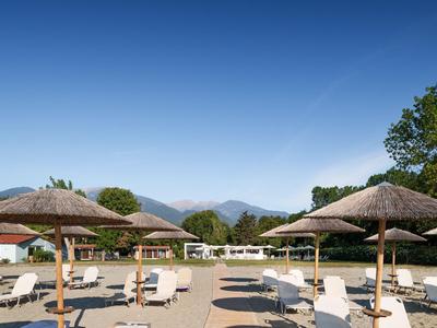 Hôtel de plage avec parasols, chaises longues et montagnes en arrière-plan sous un ciel dégagé.