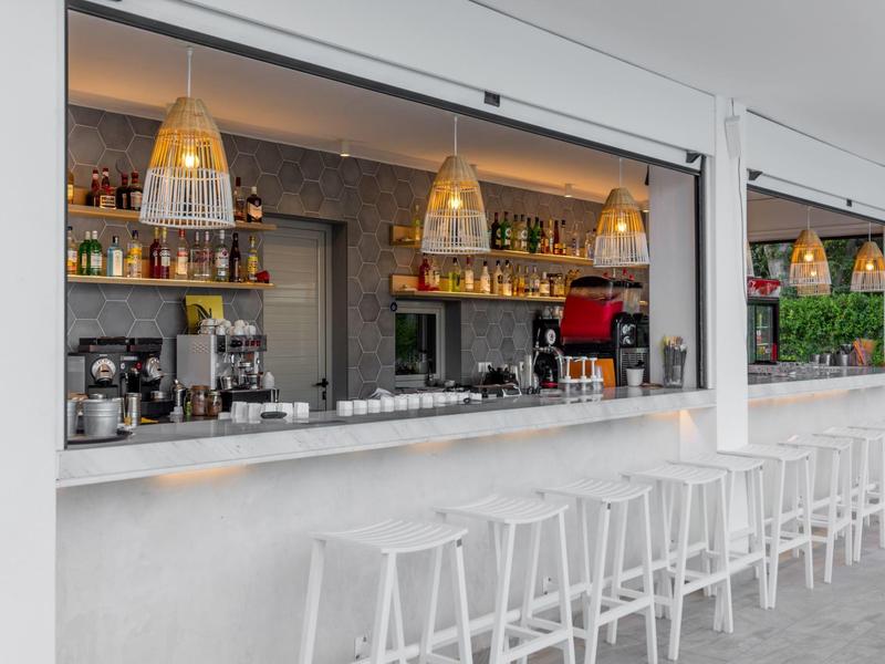 Modern outdoor bar area with white stools and pendant lights.