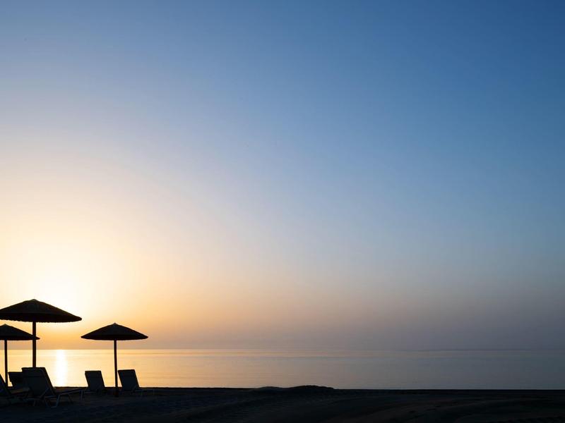 Three lounge chairs under umbrellas on a quiet beach at sunset.