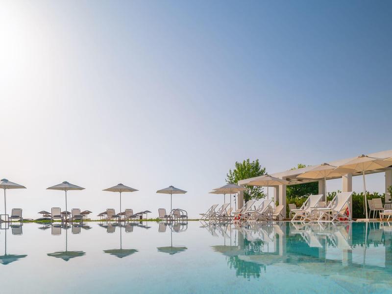A calm pool with sun loungers and umbrellas under a clear sky.