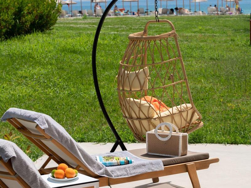 Lounge chairs and a round hanging chair on the beach with a view of the blue sky.