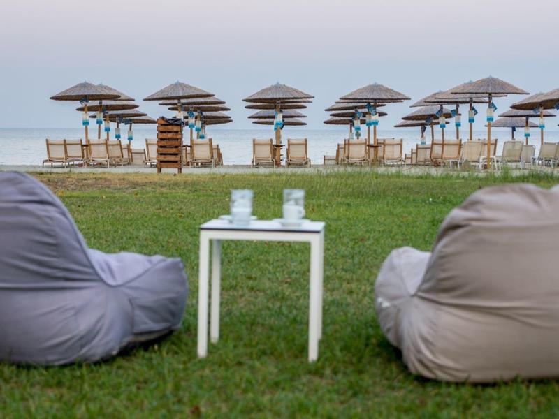 Two fabric bean bag chairs with small table on grass facing beach umbrellas