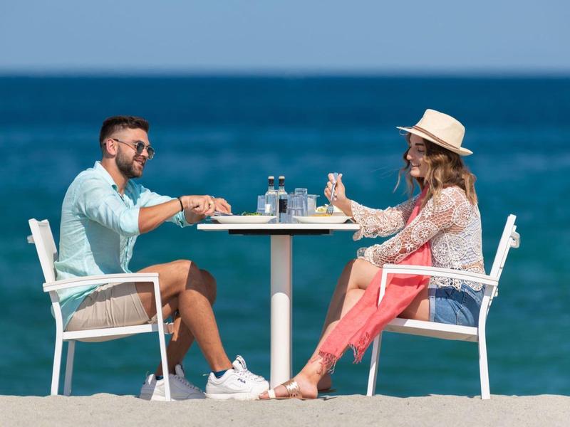 Couple at a table on the beach with sea in the background and drinks on the table.