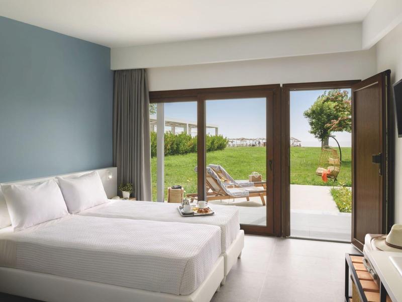 Modern hotel room with double bed, terrace view, and garden with lounge chairs.