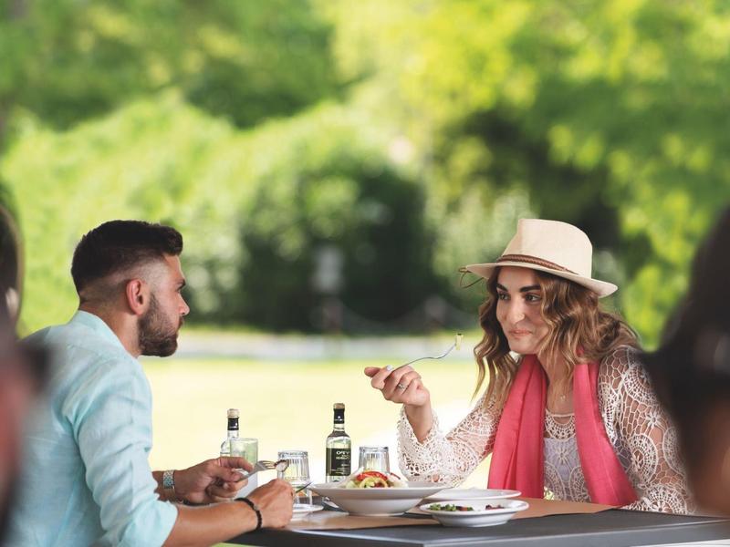 Two people casually chatting over drinks and snacks outdoors with green background.