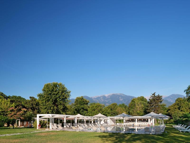 Open-air restaurant with white pergolas and tables against mountains and blue sky