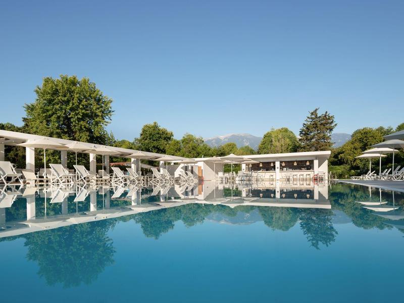 Large pool with white lounge chairs and umbrellas under clear sky.