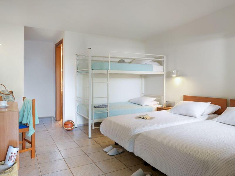 Bright hotel room with bunk bed and two single beds on tiled floor.