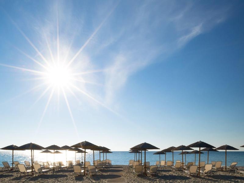 Beach with sun umbrellas and chairs under bright sunshine over the sea.