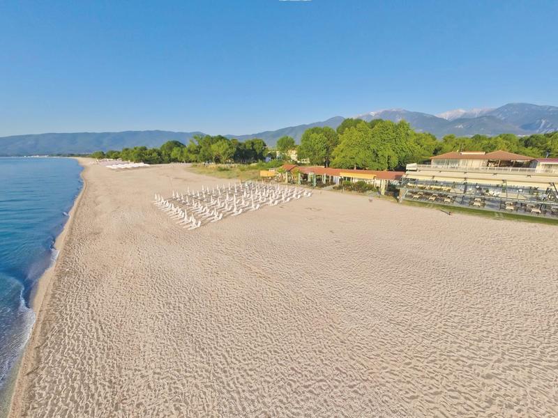 Wide sandy beach with lounge chairs and adjacent hotel near wooded hills