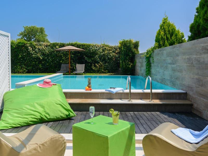 Outdoor pool area with loungers, small table, beanbag, and umbrella against a clear sky.