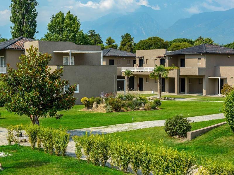 Modern houses surrounded by green lawns and trees under a blue sky with clouds.
