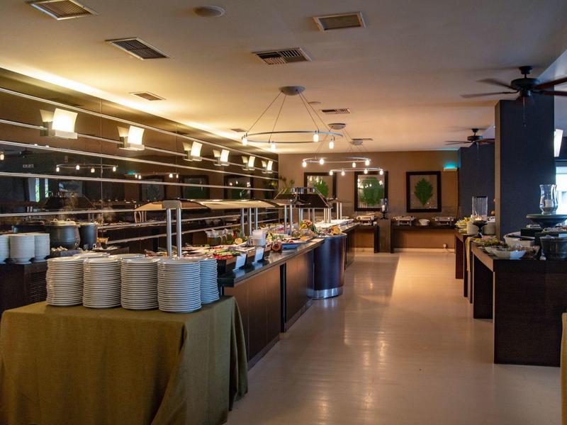 Spacious hotel buffet with stacked plates, food counters, and warm lighting.