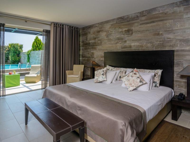 Modern hotel room with large bed, wooden accent wall, and sliding doors to a pool area.