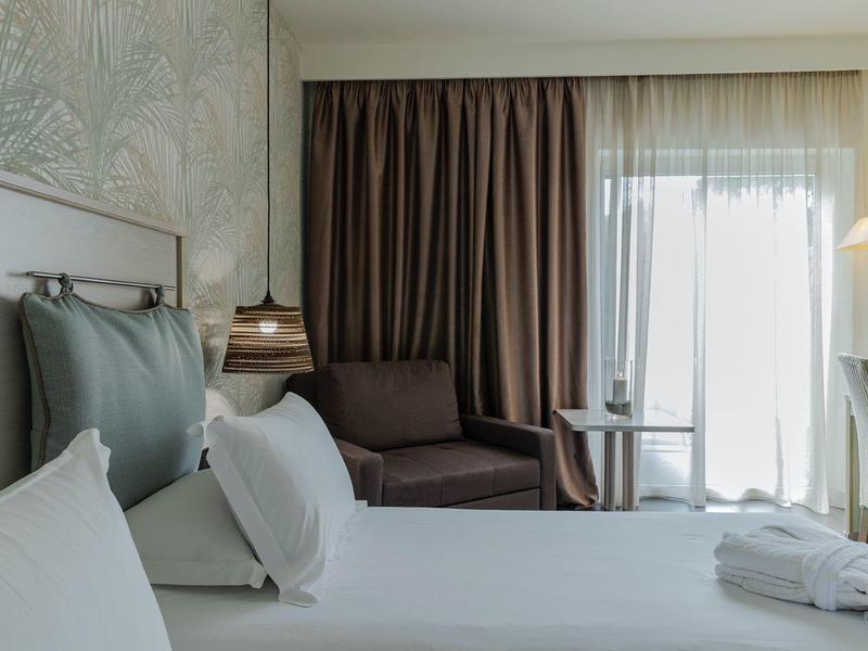 Modern hotel room with a bed, armchair, pendant light, and window covered with curtains.