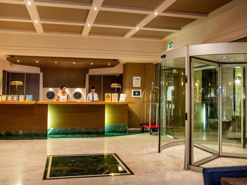Hotel lobby with reception desk, staff, revolving door, and warm lighting.