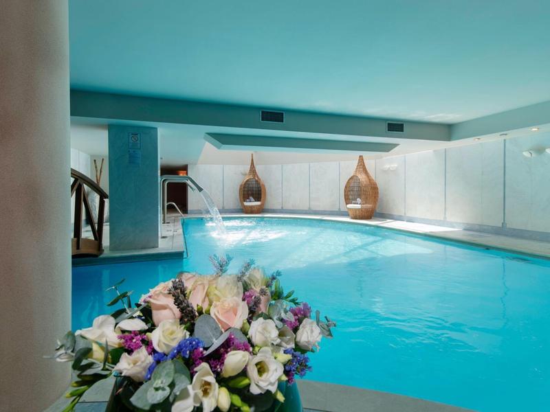 Indoor pool with bright blue water and white walls, decorated with a flower bouquet in the foreground.