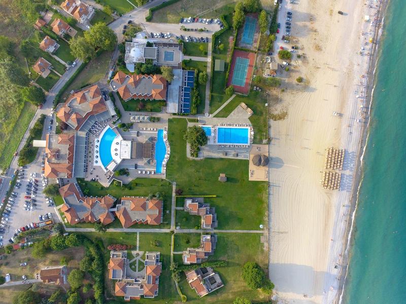 Aerial view of a beachfront resort with pools, tennis courts, and sandy beach by the ocean.