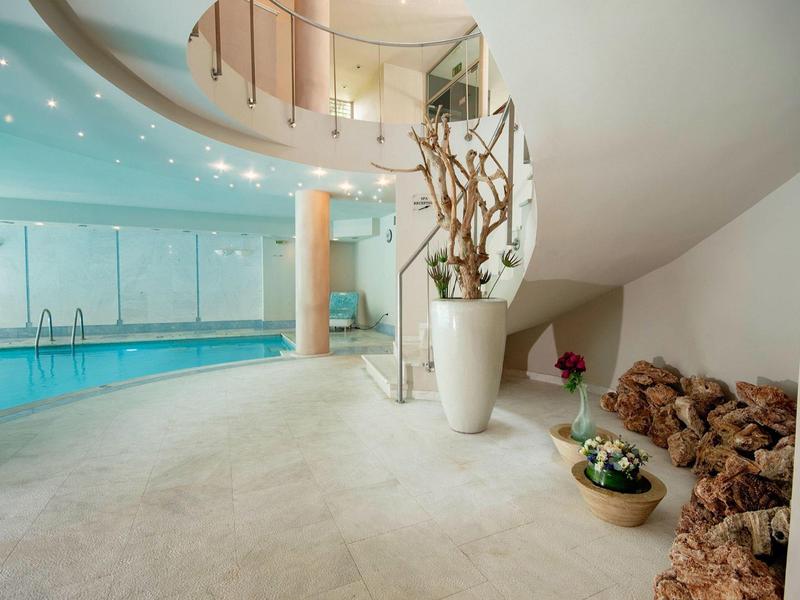 Spacious indoor pool area with a curved wall, large vase with branches, and decorative stones.