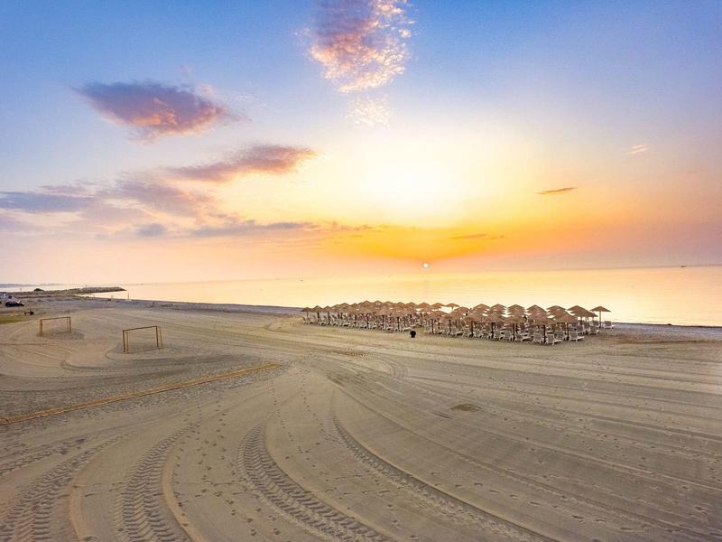 Empty sandy beach with rows of sun umbrellas during a colorful sunset.