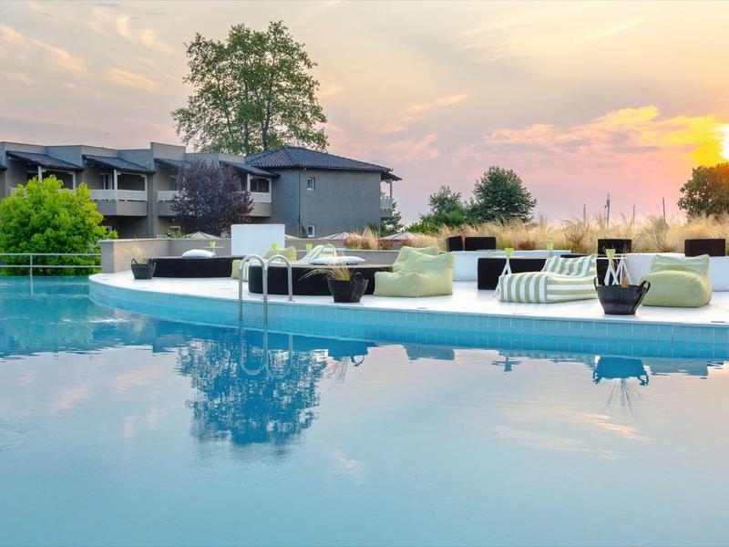 Modern outdoor pool at sunset with loungers and resort buildings in the background.