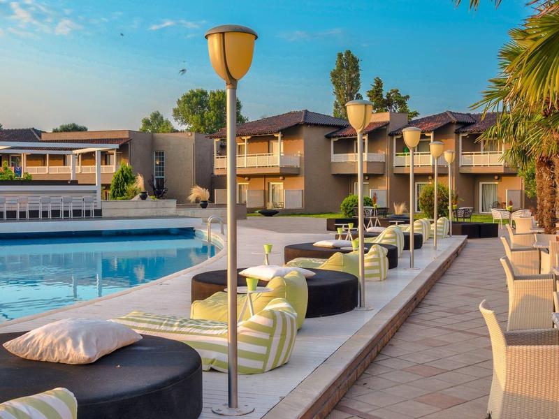 Luxurious outdoor pool area with modern seating, palm trees, and two-story hotel buildings at sunset.
