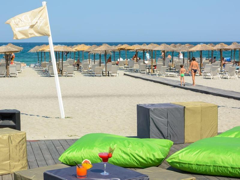 Beach scene with green bean bags, wooden pallets, umbrellas, and a calm sea under clear sky.