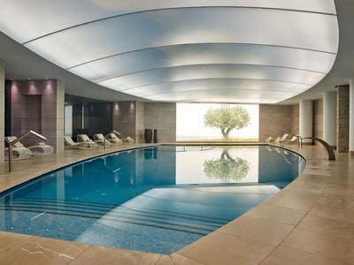 Innenpool mit modernen Liegen und indirekter Beleuchtung neben einer großen Fensterfront mit Blick auf einen Baum.